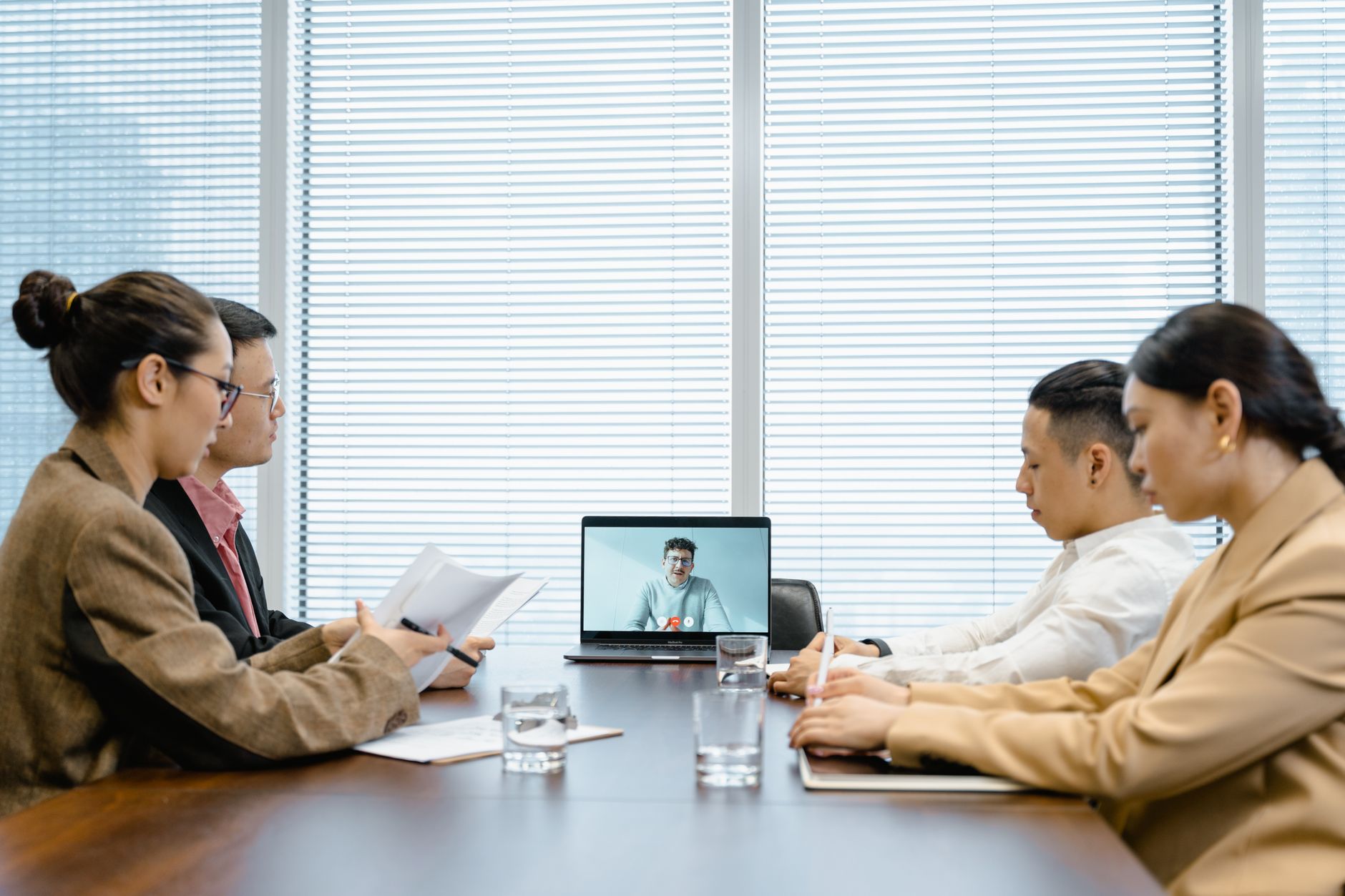 Four colleagues in a conference room speaking with a remote teammate on a video call