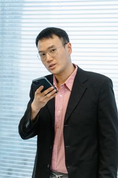 Asian businessman in suit using smartphone for communication in an office setting.