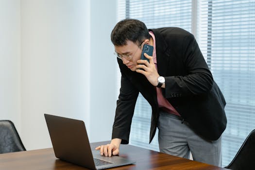 Asian businessman in the office multitasking with a laptop and smartphone call.