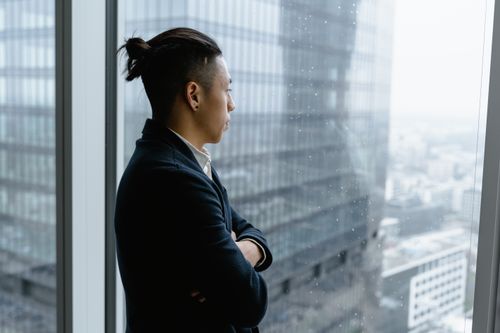 Free Asian businessman in formal attire looks out from office window on a rainy day. Stock Photo