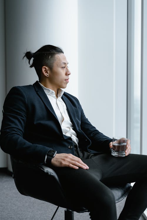 A Businessman Sitting on a Chair while Holding a Glass of Water