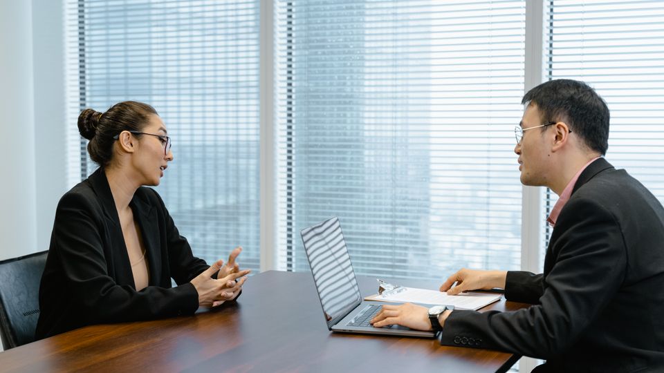 Two Asian professionals in an interview conversation at an office table.
