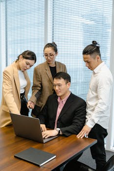 A diverse team collaborates around a laptop in a modern office setting.