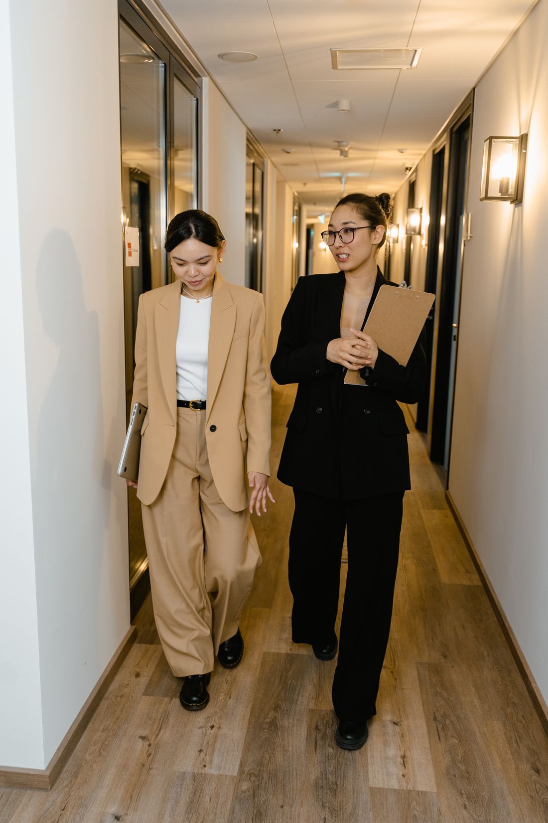 Two colleagues walking and talking down a bright office corridor. Photo by MART PRODUCTION on Pexels