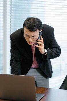 Focused businessman multitasking with a call and laptop in a modern office setting.