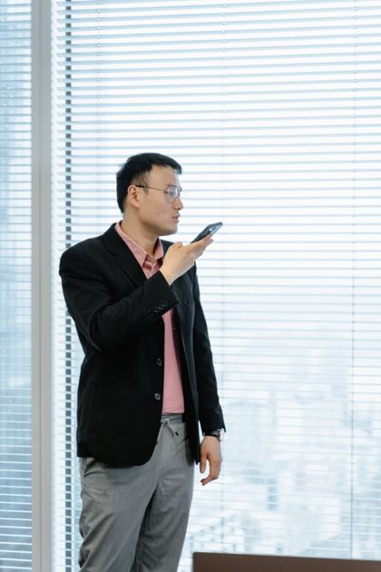 Homme en tenue professionnelle utilisant une commande vocale sur smartphone dans un bureau
