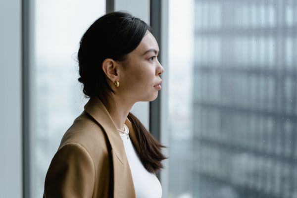Woman in business attire looking thoughtfully out a window, weighing a decision