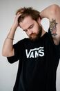 Concentrated young tattooed bearded male with closed eyes in trendy t shirt touching head on light background