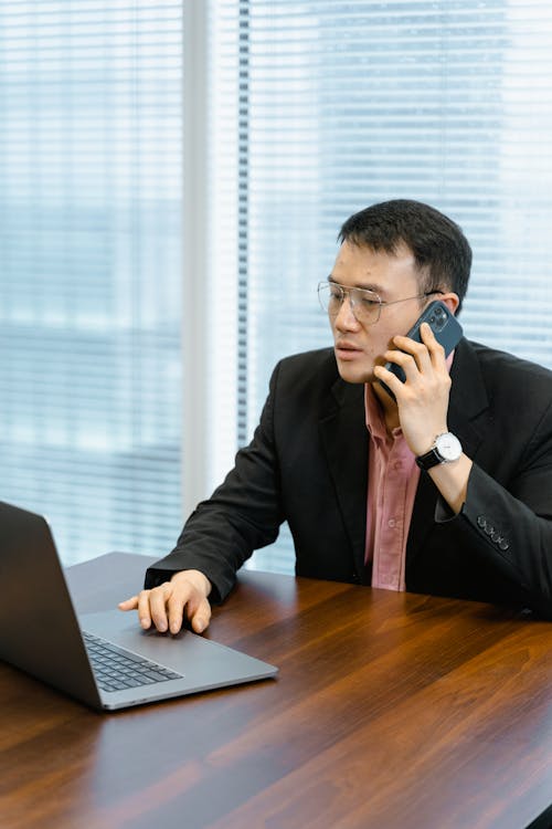 Free Man in Glasses Talking on the Phone While Using Laptop Stock Photo