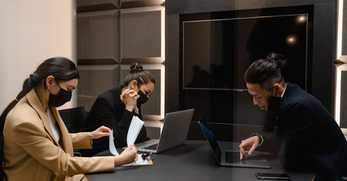 Asian business professionals collaborating in office with laptops and documents during meeting.