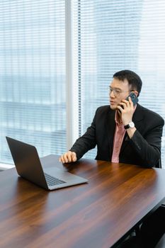 Businessman using smartphone in modern office, working with laptop.