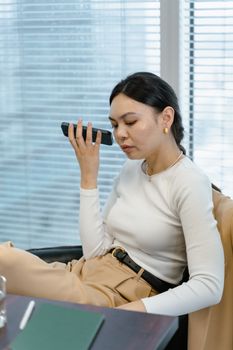 Young businesswoman using voice command on smartphone in modern office.