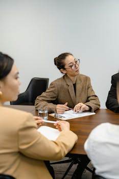Three business professionals in a collaborative meeting at a wooden table in an office setting.