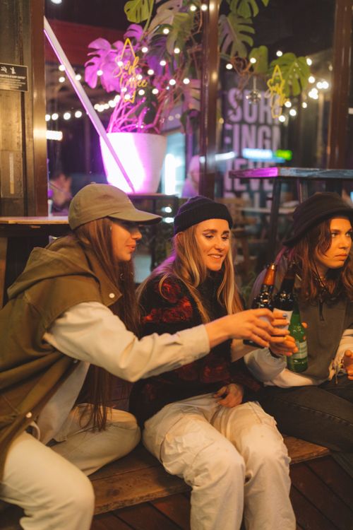 Free Three young women sitting and sharing drinks at a lively bar environment. Stock Photo