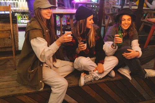 Free Three stylish young women enjoy beverages while sitting together outdoors. Vibrant and friendly atmosphere. Stock Photo