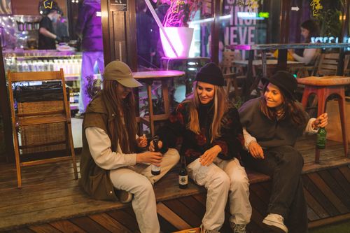 Free Three young women enjoying a casual evening with drinks on an outdoor patio. Stock Photo