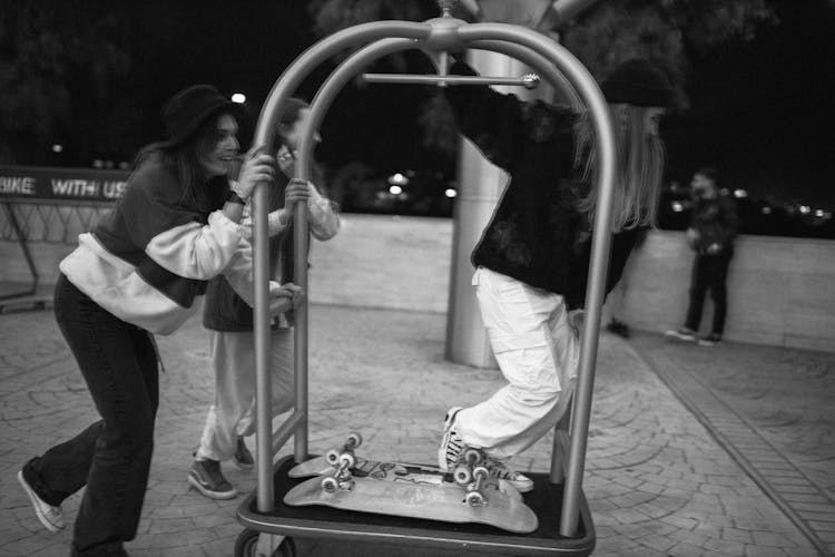 Grayscale Photo Of Friends Playing With The Hotel Bell Cart