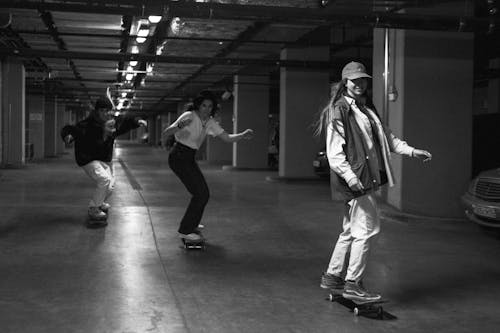 Black and White Photo of Women Using Skateboards in a Parking Area