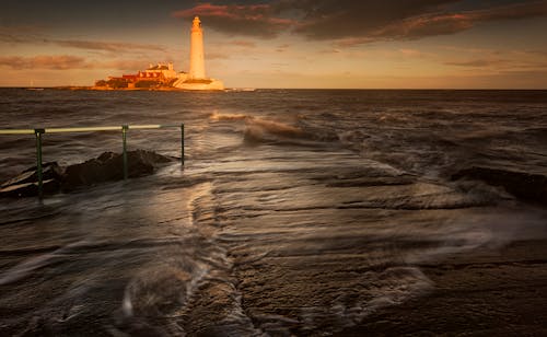 White Lighthouse Near Body of Water during Sunset