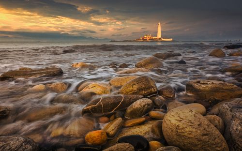 Free Rocky shore with St Mary's Lighthouse at sunset, capturing dramatic oceanic scenery. Stock Photo