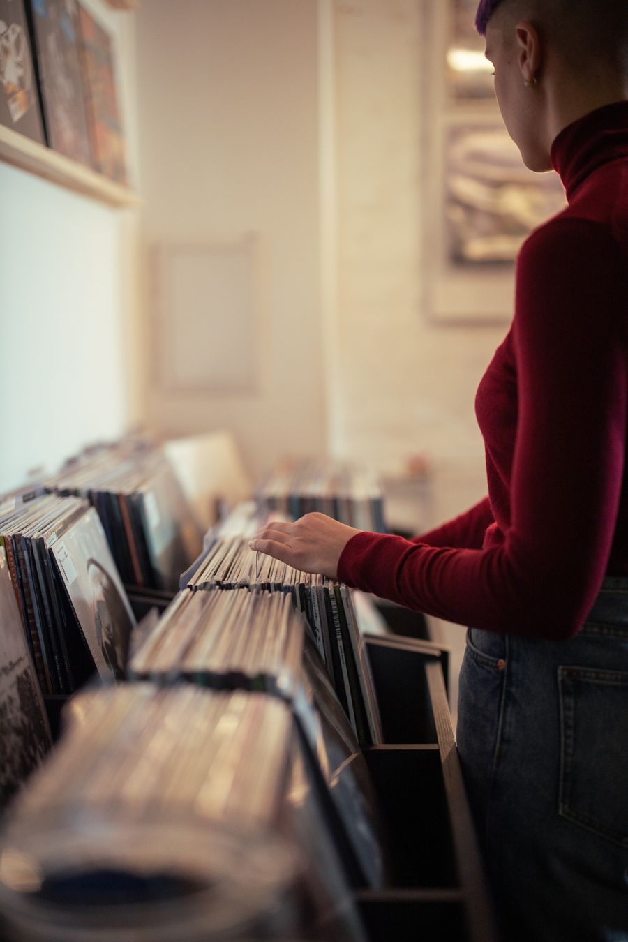 Blurred record-shop interior, a shopper in a red turtleneck flipping through crates — photo by cottonbro studio on Pexels