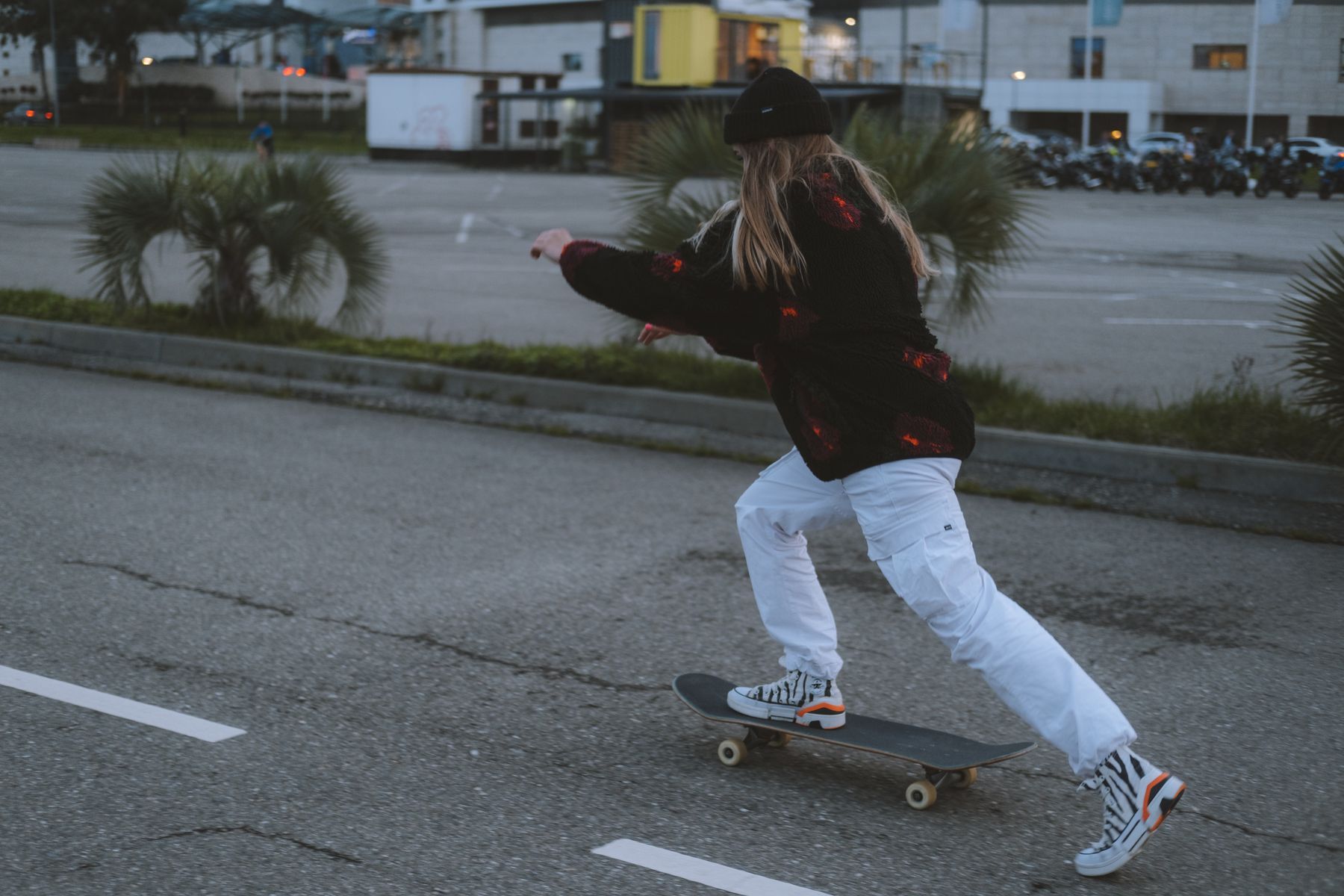 Woman wearing a black beanie while skateboarding through a city street at dusk
