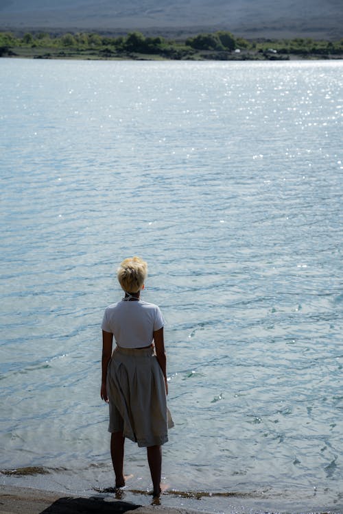 Woman in White Shirt and Skirt Standing on Sea Shore