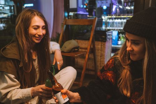 Free Two young women toasting with beer bottles in a cozy indoor bar setting. Stock Photo