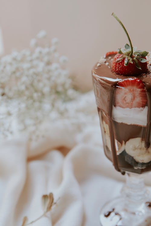 Free Glass of appetizing chocolate dessert with strawberries ans bananas served on banquet table decorated with satin cloth and bunch of delicate flowers Stock Photo