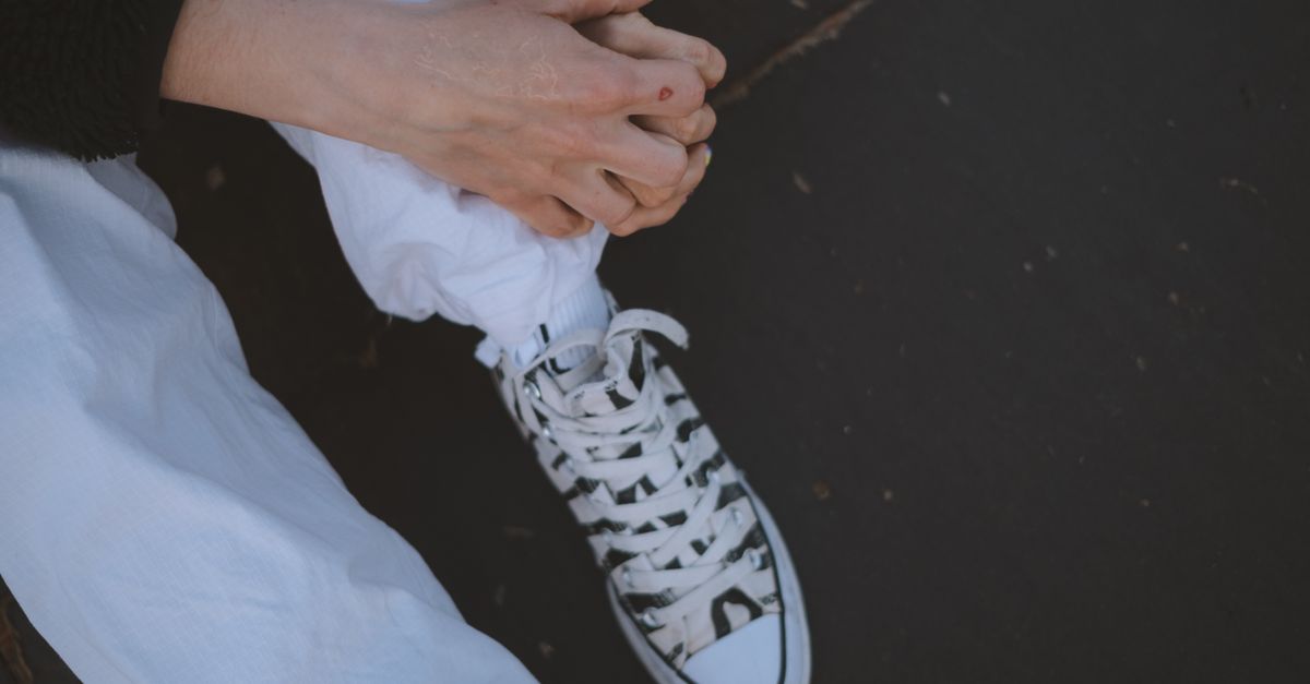 Detailed view of clasped hands and sneakers in an urban environment.