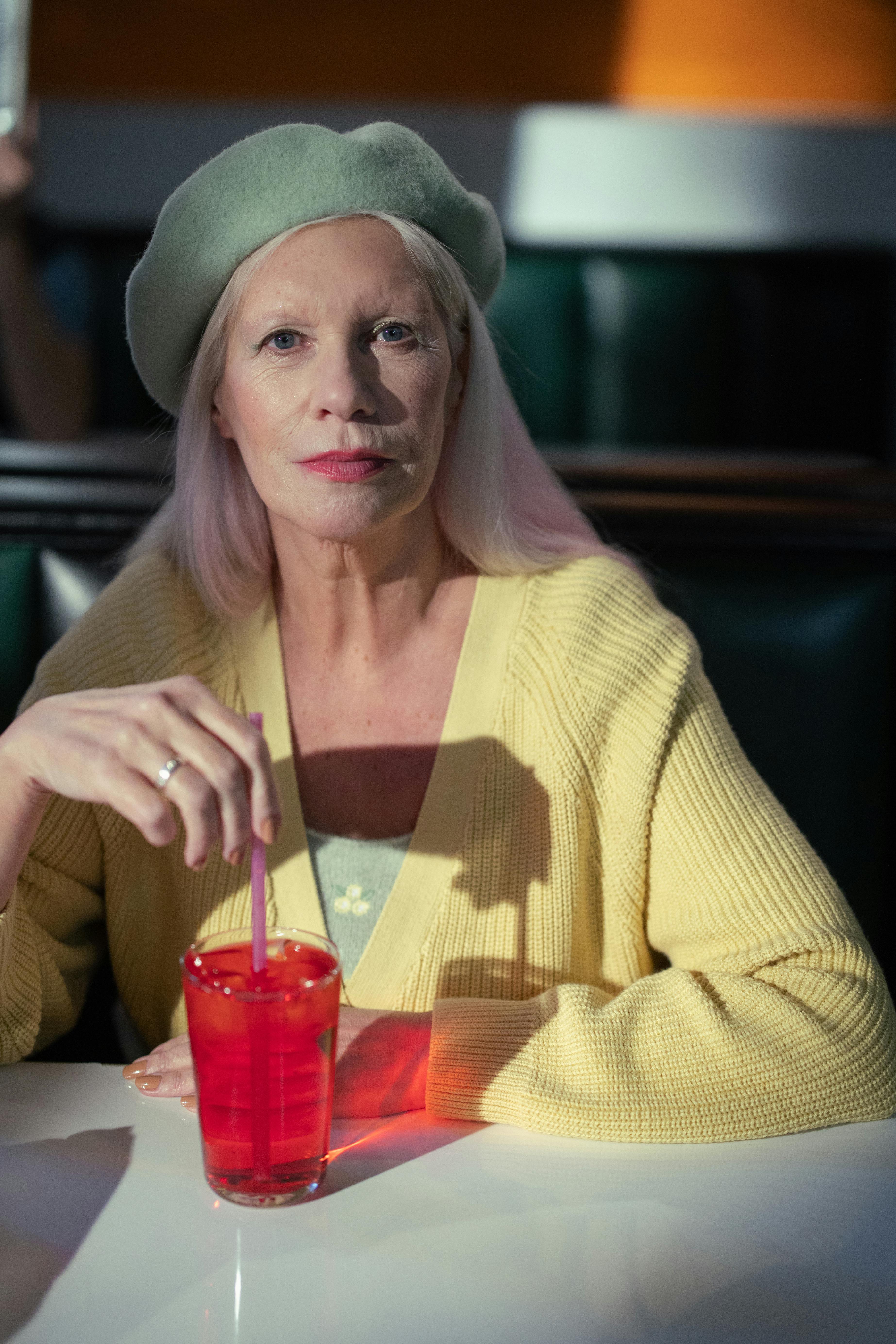 Elderly fashionable woman with chic beret enjoying a drink in a café setting.