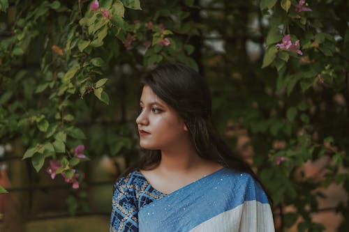 Side View of a Woman Standing Near Trees with Flowers
