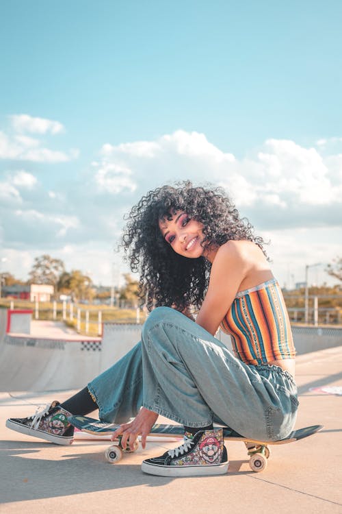 Free A Woman with Curly Hair Sitting on a Skateboard Stock Photo