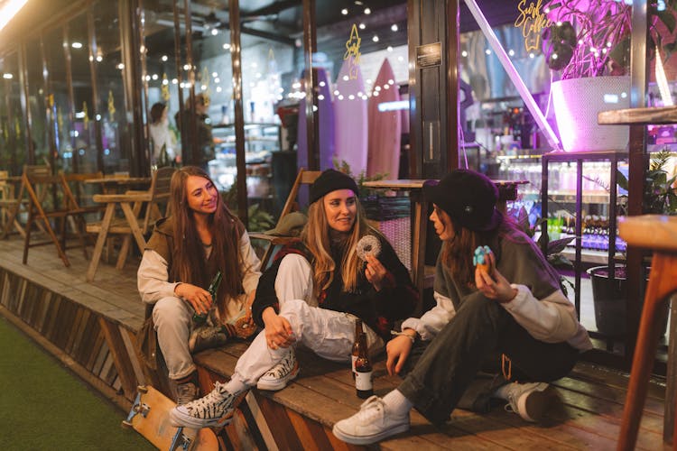 Women Sitting On The Wooden Floor Of The Restaurant Eating Donuts