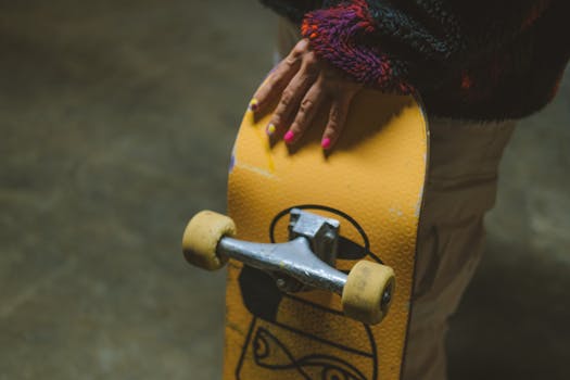 A detailed view of a painted hand grasping a yellow skateboard indoors.