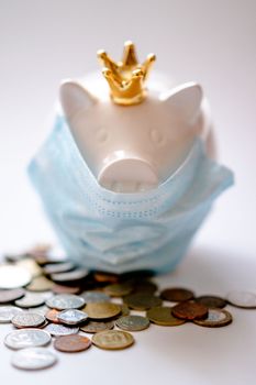 Money box with crown and protective mask among coins representing concept of saving money during COVID pandemic