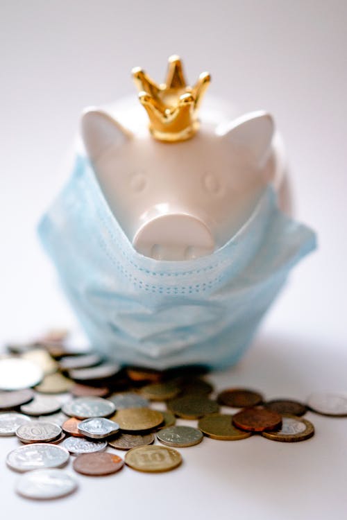 Free Money box with crown and protective mask among coins representing concept of saving money during COVID pandemic Stock Photo