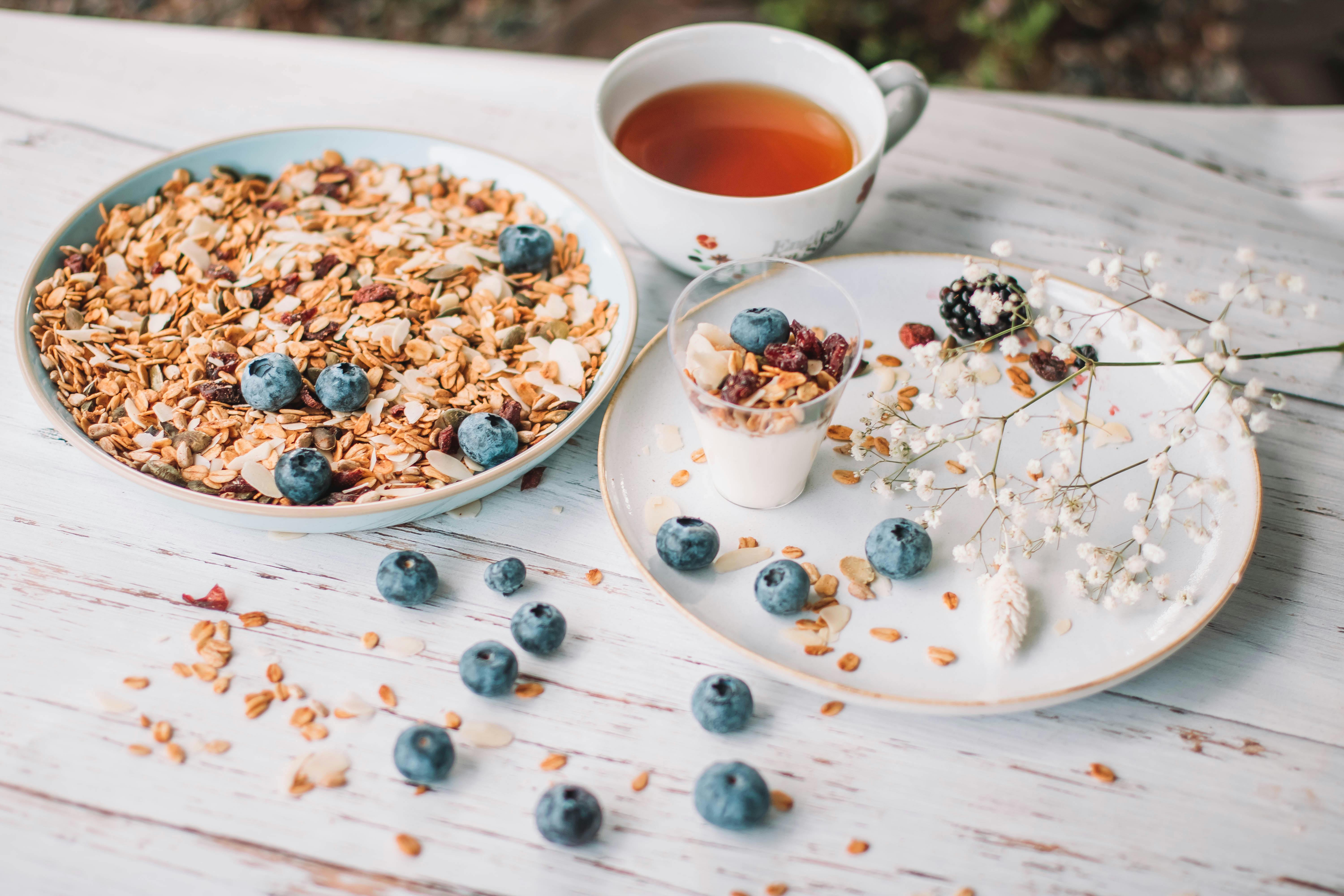From above of tasty granola placed near plate with yogurt verrine with granola on wooden table with cup of tea and twig