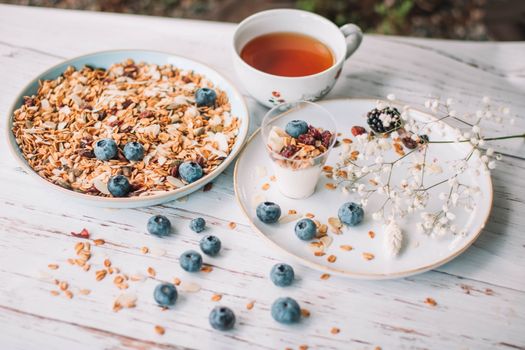 From above of tasty granola placed near plate with yogurt verrine with granola on wooden table with cup of tea and twig