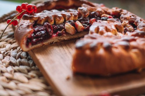 Free Delicious cut pie with berry filling placed on chopping board with red currant on wicker mat in light room on blurred background Stock Photo