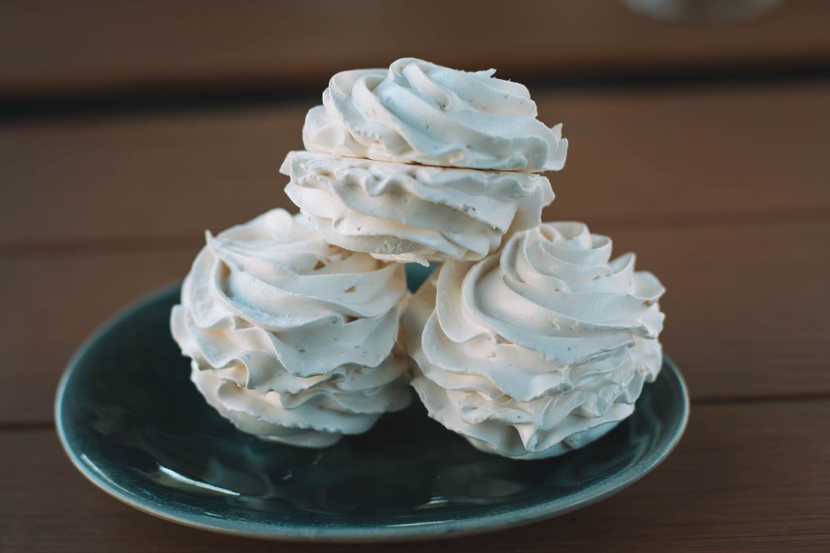 Heap of tasty sweet fresh zephyr with creative geometric pattern served on green ceramic plate on wooden planks on terrace