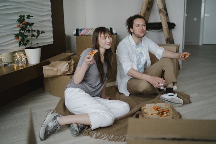 A Couple Sitting On The Floor Eating Pizza