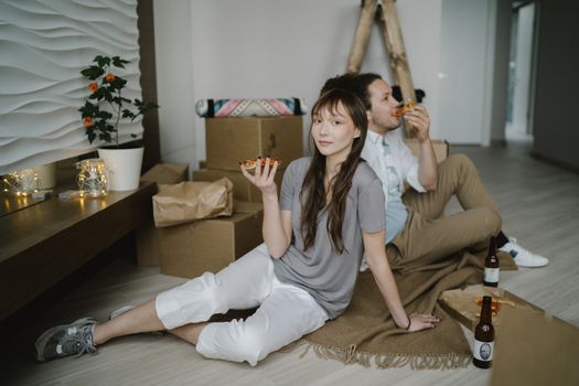 Couple enjoying pizza and beer while unpacking in their new apartment.