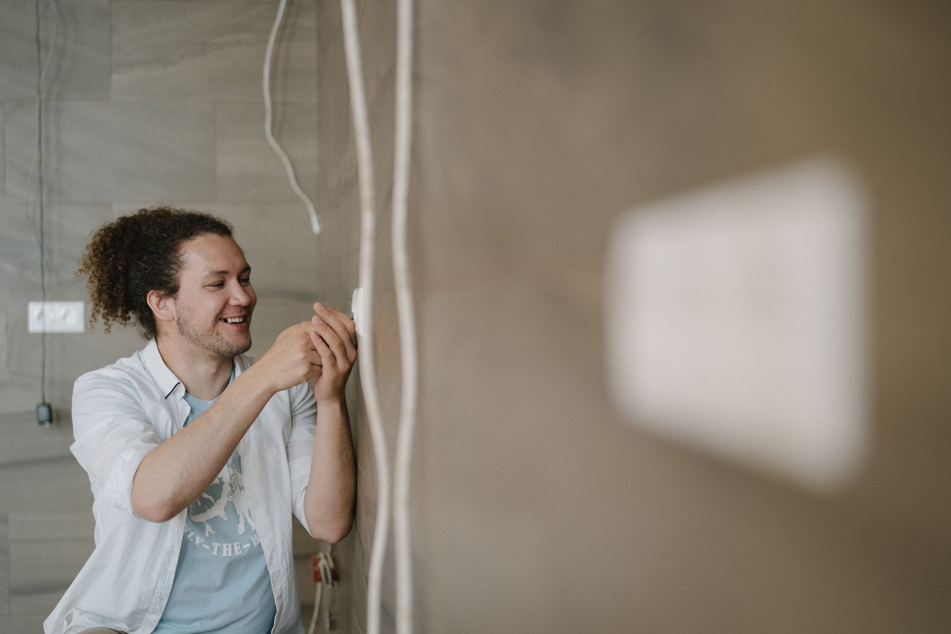 Nick's Electrical LLC - An electrician with curly hair adjusts an outlet indoors, smiling as he works.