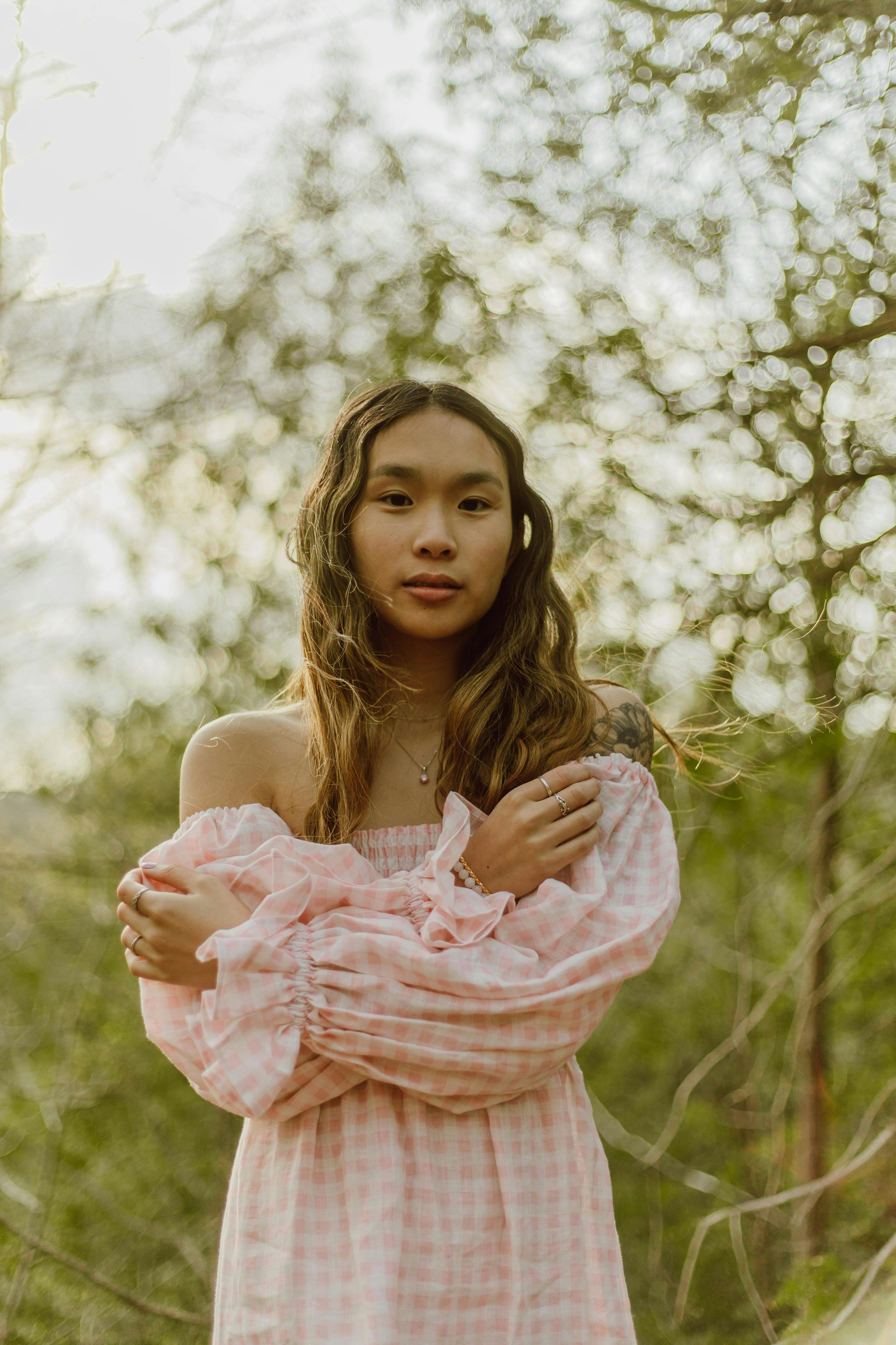 A serene outdoor portrait of a young woman in a pink checkered dress surrounded by greenery.