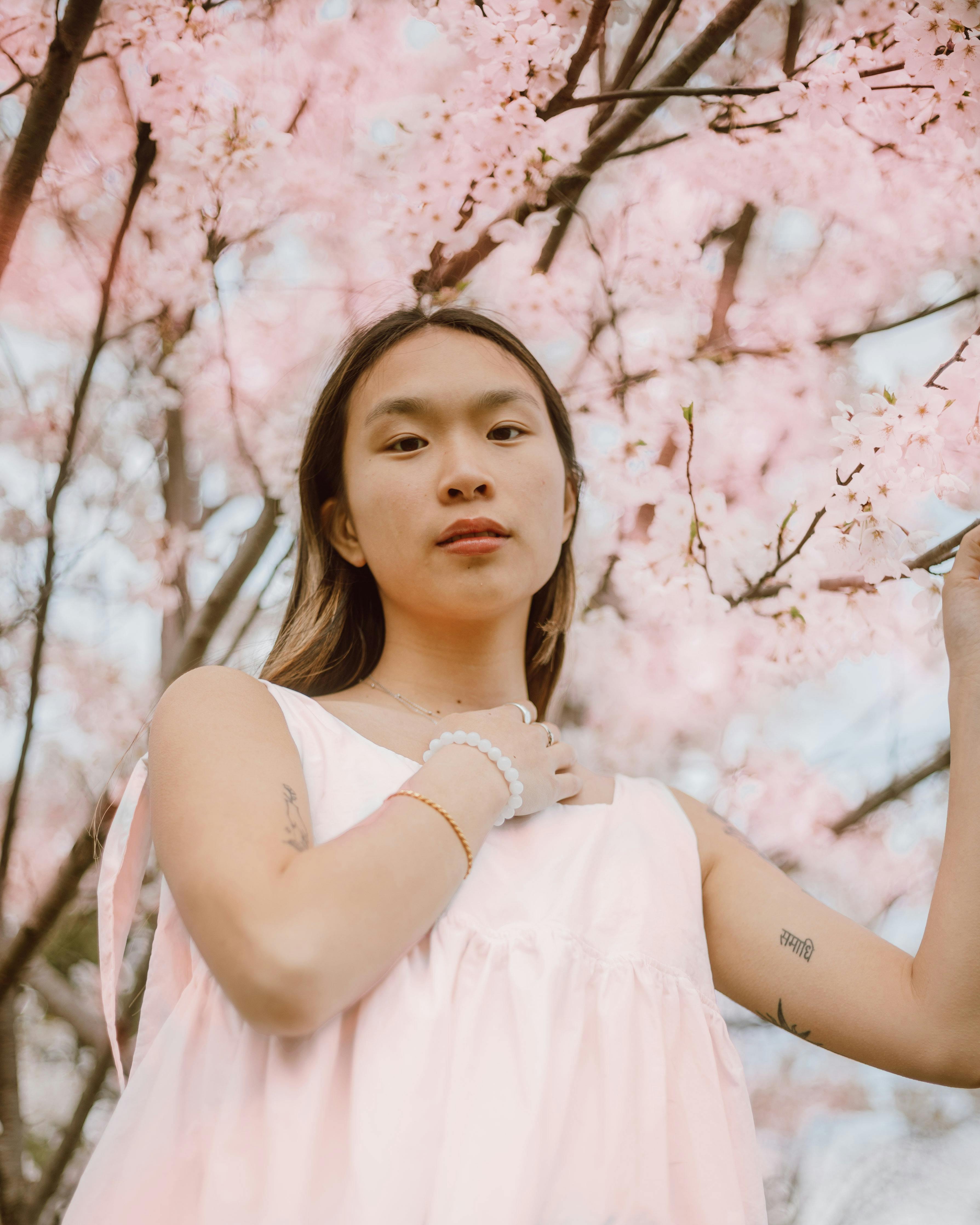 gentle asian teen with tattoos under blooming sakura tree