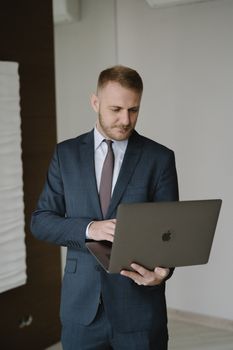Caucasian man in a suit using a laptop in a modern indoor office setting.