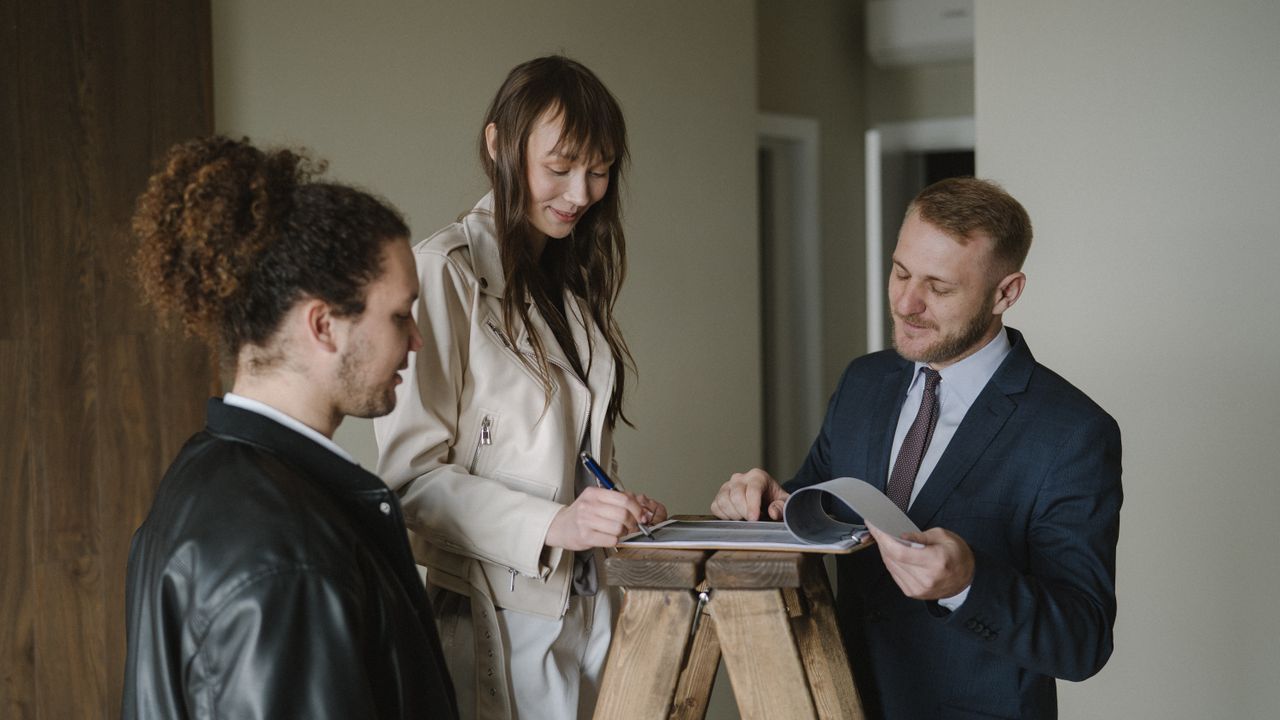 A couple signing real estate documents with a realtor inside a new apartment.