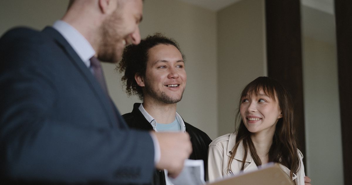 Casal jovem e feliz conversando com um corretor dentro de um apartamento novo.
