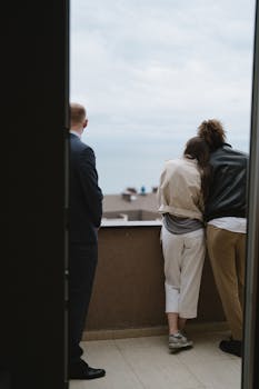 Couple leaning on balcony with realtor viewing new home landscape.